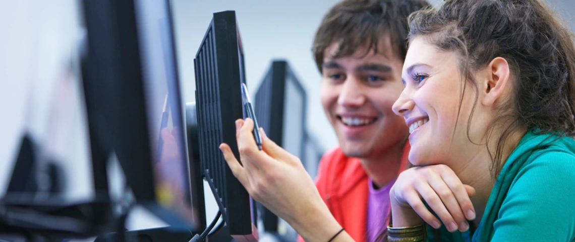 Two smiling students sitting in front of a computer